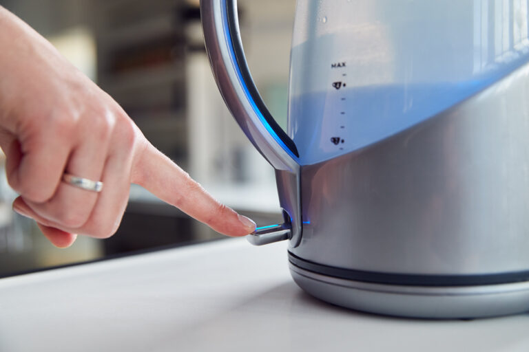 Close Up Of Woman Pressing Power Switch On Electric Kettle To Save Energy At Home