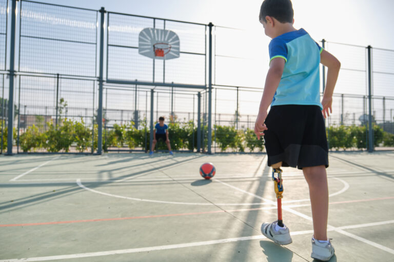 Two friends playing football, one has a leg prosthesis and is kicking a penalty.